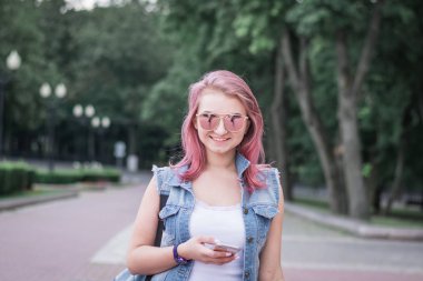 Modern saç modeli Ile genç kentsel kadın bir kentsel park sokakta yürüyüş Smartphone kullanarak