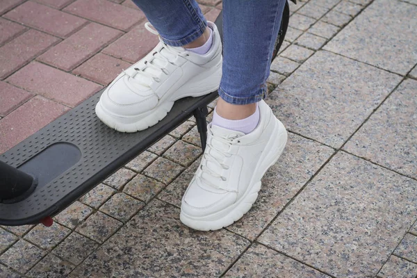 Les jambes de la fille au premier plan et les jambes des gars en arrière-plan vêtus de chaussures en cuir et debout à côté des scooters électroniques noirs — Photo
