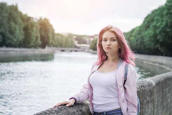 Joven mujer sosteniendo mochila mientras de pie contra el río de la ciudad —  Fotos de Stock