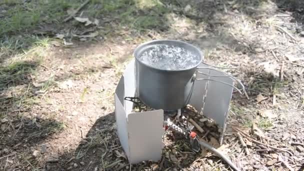 Água fervente em um pequeno pote de acampamento com uma tocha de gás em miniatura — Vídeo de Stock