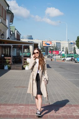 şık genç kadın sokakta yürüyor ve telefonda konuşuyor