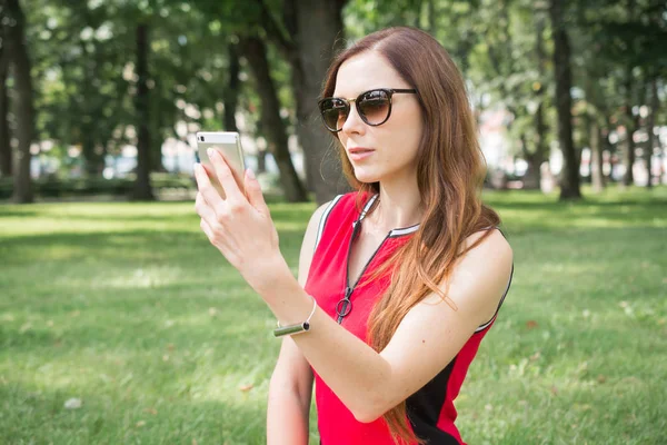 parkta açık havada dinlenirken cep telefonu ön kamera kendini fotoğraf çekmek rahat giyim güzel kadın