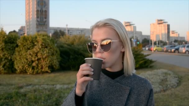Porträt einer jungen schönen blonden Hipsterfrau, die auf dem herbstlichen Parkhintergrund posiert und trinkt — Stockvideo
