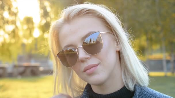 Junge schöne blonde Frau Nahaufnahme Porträt lächelnd und Blick in die Kamera mit Wind im Haar im Freien — Stockvideo