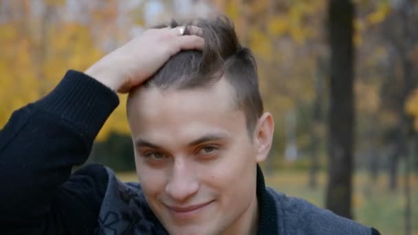 Close-up retrato de belo jovem ao ar livre, olhando para a câmera e tocando seu cabelo — Vídeo de Stock