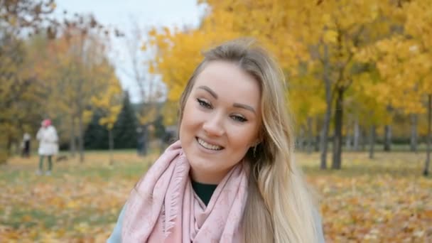 Autumn outdoor Portrait of a beautiful young blonde woman smiling and looking at the camera — Stock Video