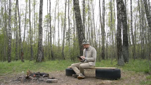 Un homme seul est assis dans la forêt et regarde la tablette — Video