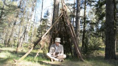 Adam ormanda derme çatma bir barınakta oturuyor ve bir yaz günü tabletindeki bir şeye bakıyor.