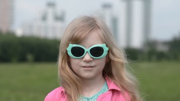 Retrato de una niña de cinco años en gafas de sol en un parque de la ciudad — Vídeos de Stock