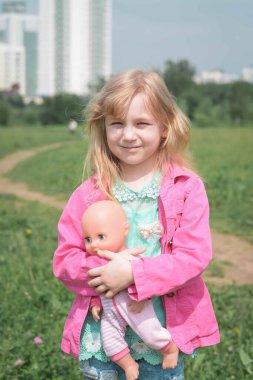 Küçük kız bir yaz günü bebeğini dışarıda tutuyor.