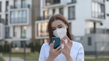Koruyucu maskeli kadın doktor akıllı telefonuna bir mesaj yazıyor.