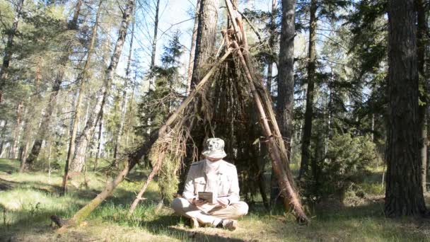 Человек в защитной маске сидит в лесу и общается через планшет — стоковое видео