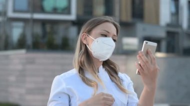 Koruyucu maskeli genç kız telefona bakar ve caddedeki saçları düzleştirir.