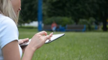 Yeşil çimenlerin arka planında tablet bilgisayarda yazan kadın eller