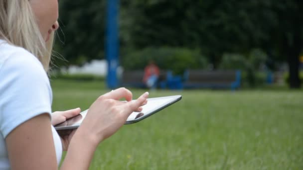 Руки женщины печатают на планшетном компьютере на фоне зеленой травы — стоковое видео