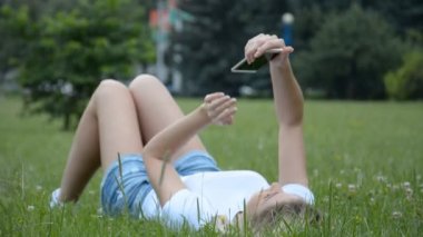 Çimlere uzanmış, cep telefonu kullanan hoş bir genç kadın.