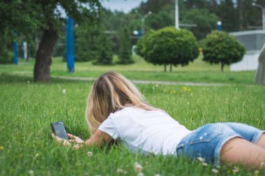 Bir kadının arka plan görüntüsü telefon mesajlarıyla çimlere uzanır ve bir yaz günü yazar.