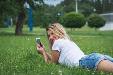 Bir kadının arka plan görüntüsü telefon mesajlarıyla çimlere uzanır ve bir yaz günü yazar.
