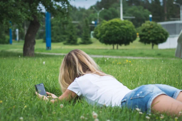 Bir kadının arka plan görüntüsü telefon mesajlarıyla çimlere uzanır ve bir yaz günü yazar.