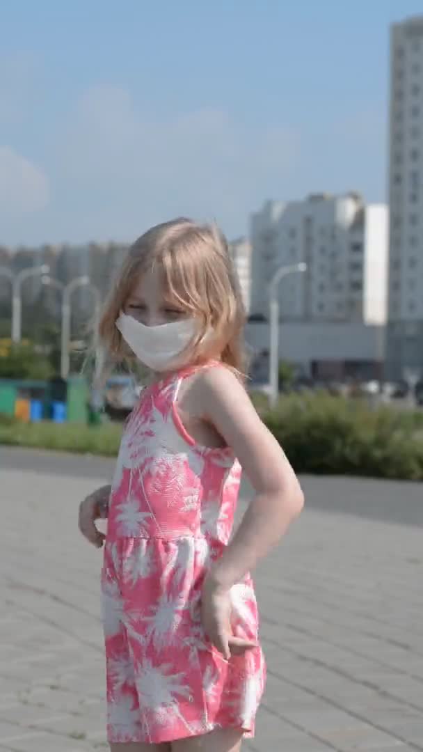 Вертикальный видеоклип маленькой девочки в розовом платье и защитная маска на лице, профилактика коронавируса — стоковое видео
