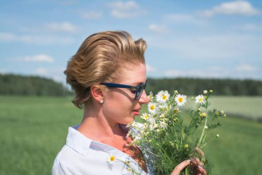 Yeşil bir tarlada elinde bir buket papatyayla güzel bir kadının portresi.