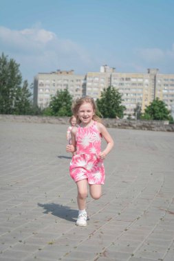 Şirin küçük kız bir yaz günü sokaklarda koşuyor ve eğleniyor.