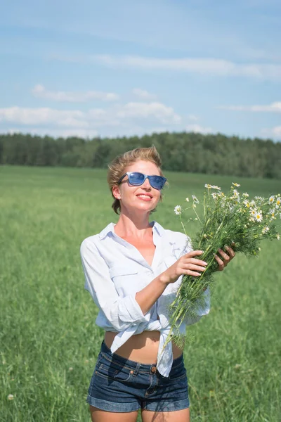 Vacker flicka på ett fält med en bukett av fältprästkragar — Stockfoto