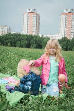İki kız kardeş parkta çimlerin üzerinde oynuyorlar.