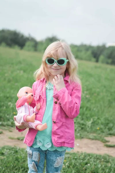 公園の小さな美しいブロンドの女の子の肖像画夏の日に人形を手に — ストック写真
