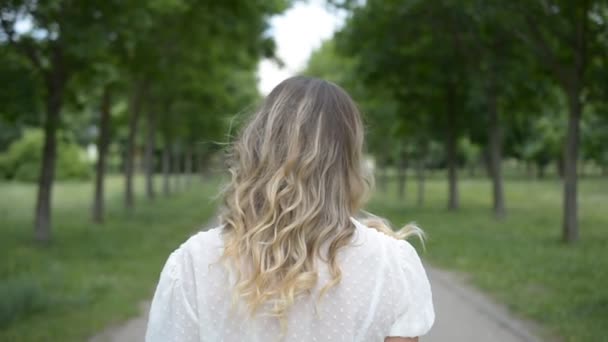 Rückenansicht des Kopfes eines blonden Mädchens, das langsam auf einem Fußweg in einem Sommerpark geht — Stockvideo