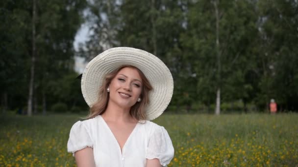 Κομψό κορίτσι πορτρέτο σε ένα μεγάλο λευκό καπέλο κοιτάζοντας την κάμερα και χαμογελώντας — Αρχείο Βίντεο