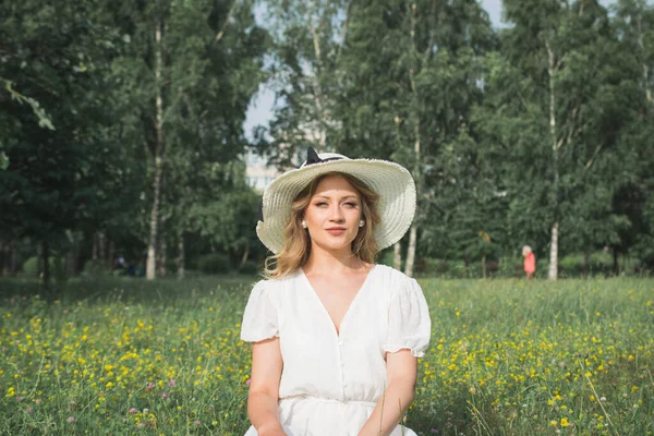 公園の写真家のための白いドレスと白い大きな帽子のポーズのエレガントな若い女の子 — ストック写真