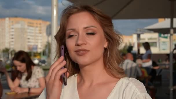 Κομψό πορτρέτο κορίτσι κάθεται σε ένα εστιατόριο το βράδυ το καλοκαίρι και μιλάμε σε ένα κινητό τηλέφωνο — Αρχείο Βίντεο