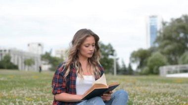 Güzel kız kampüs çimlerinde kitap okuyor.