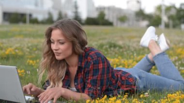 Güzel ve modern Kafkasyalı kız öğrenci ya da serbest çalışan bir dizüstü bilgisayar, kampüste yeşil çimlerde oturuyor.
