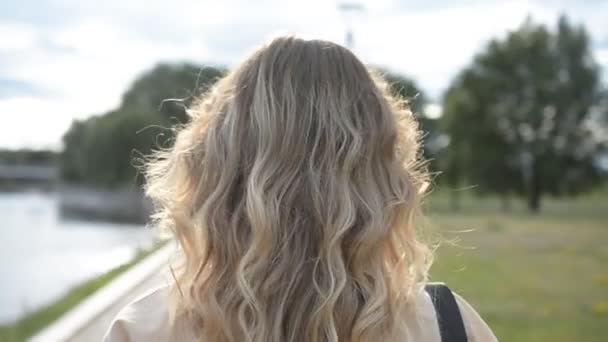 Vue arrière de l'étudiante aux longs cheveux blonds marchant jusqu'au bâtiment universitaire dans le parc — Video