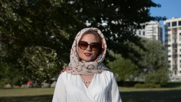 Retrato de una mujer rusa hermosa y elegante en un vestido blanco y bufanda y en gafas de sol — Vídeos de Stock