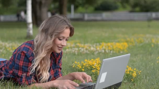 Bella ragazza caucasica sdraiata sull'erba utilizzando il computer portatile — Video Stock