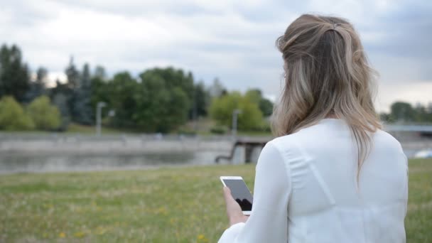 Vista posteriore della donna caucasica in abito bianco con il telefono in mano — Video Stock