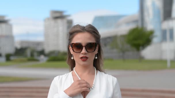 Sommar porträtt av en snygg kaukasiska flicka i solglasögon och en vit klänning, vintage frisyr, tittar på kameran — Stockvideo