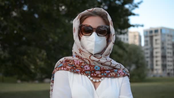 Retrato de una mujer elegante con un pañuelo en la cabeza y gafas de sol, en una máscara protectora que está mirando a la cámara — Vídeos de Stock