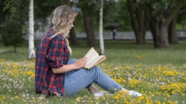 Güzel beyaz kız kampüs çimlerinde kitap okuyor.