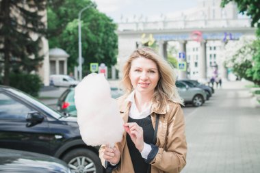 Açık havada elinde pamuk şeker tutan gülümseyen bir kızın yakın portresi.