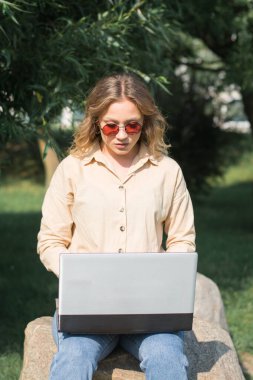 Yeşil bir parkta dizüstü bilgisayarla çalışan öğrenci kız.