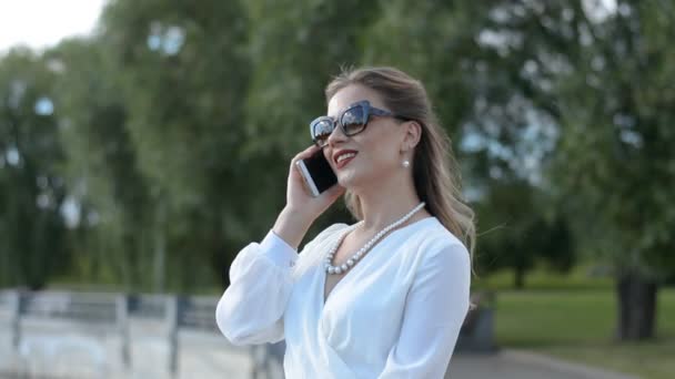 Şehir caddesinde dikilirken cep telefonuyla konuşan uzun saçlı beyaz çekici bir kız. — Stok video
