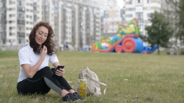 Chica universitaria sentada en el césped utilizando el teléfono móvil en el campus — Vídeo de stock