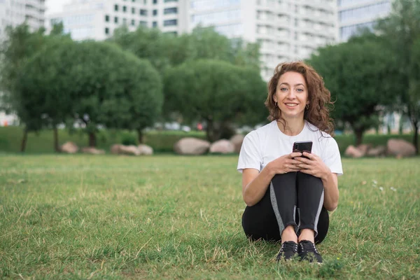 Joven Mujer Feliz Hablando Teléfono Celular Sentado Hierba Parque Ciudad — Foto de Stock