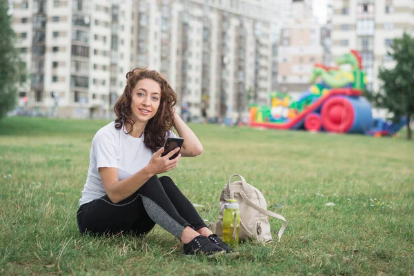 Joven Mujer Feliz Hablando Teléfono Celular Sentado Hierba Parque Ciudad — Foto de Stock