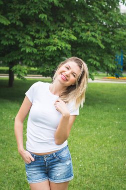 Beyaz tişörtlü ve kot şortlu güzel bir kadın yazın şehirde yürür.