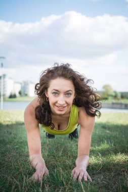 Spor yapan kadın çim egzersizleri yapıyor ve çimlerin üzerinde geriniyor.